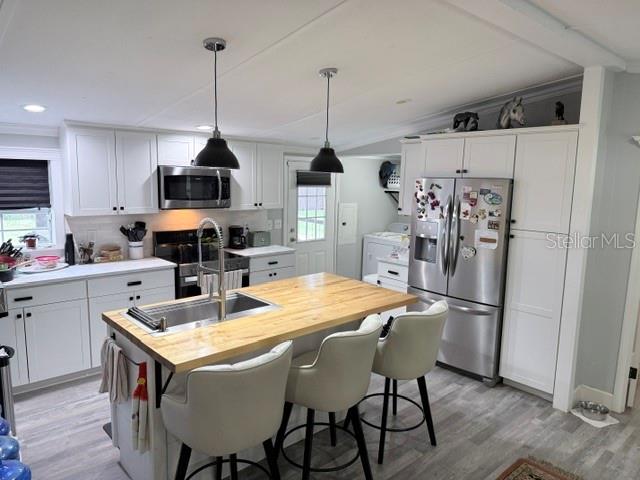 A kitchen features white cabinetry, a wooden island with three stools, and stainless steel appliances — 23065 SW 119TH PLACE, DUNNELLON, FL