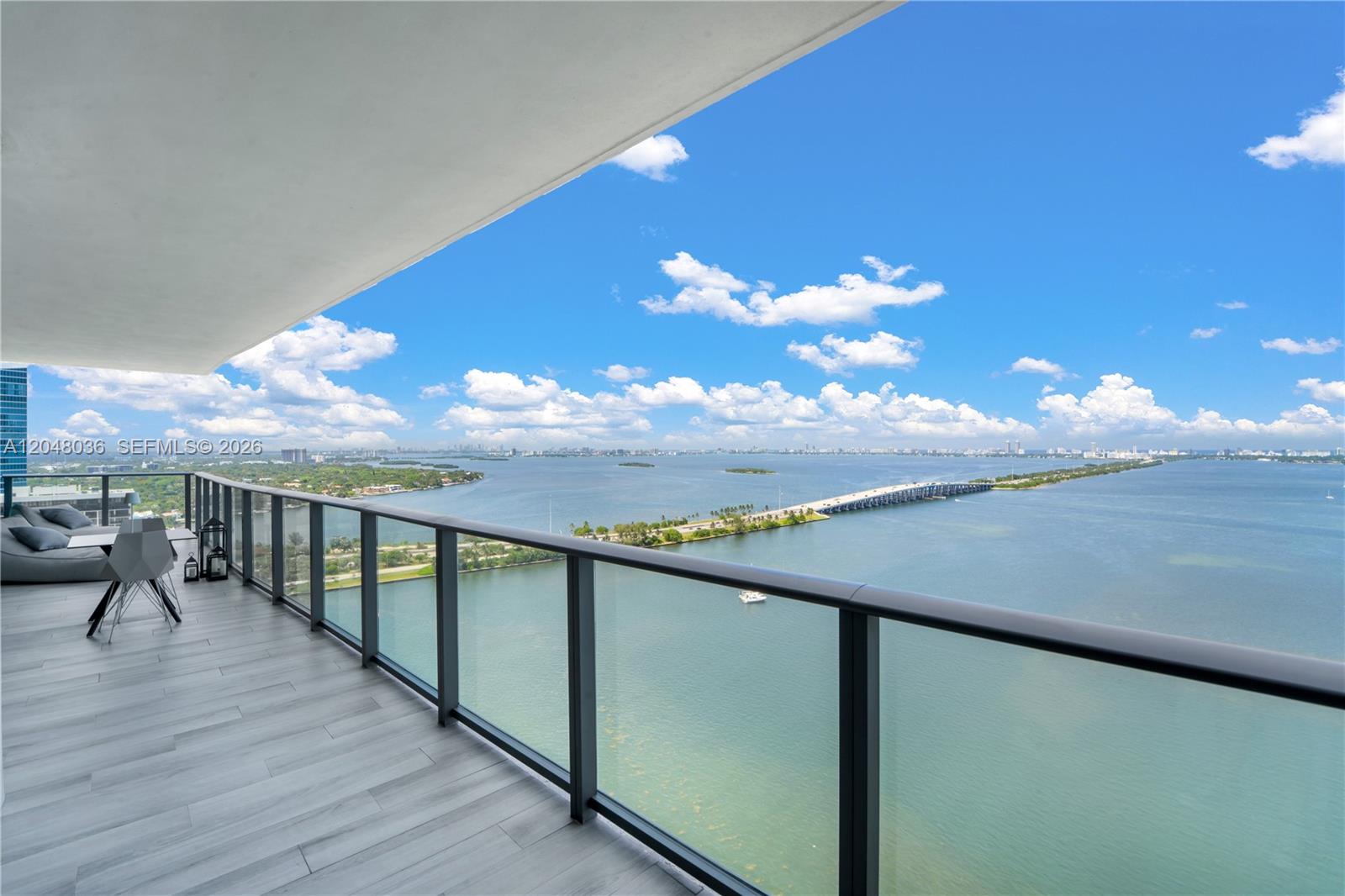 A high-rise balcony with glass railings overlooks a bay, a bridge, and a distant city — 3131 NE 7th Ave # 2706, Miami FL 33137, MIAMI, FL