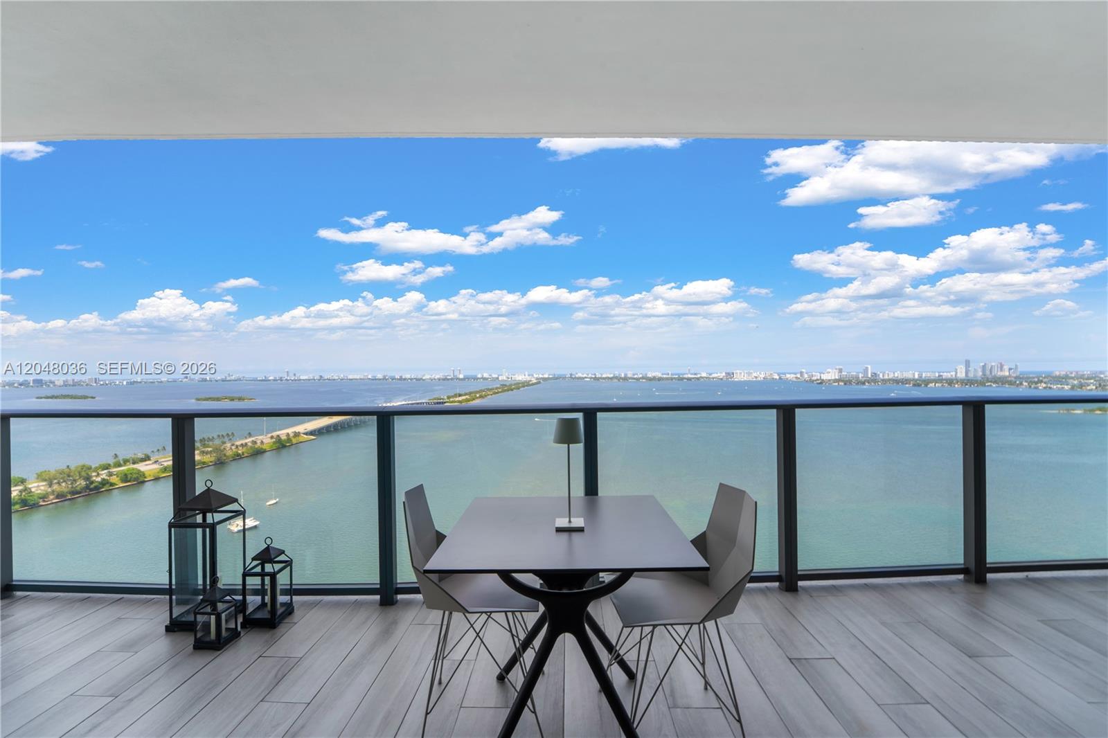 A balcony features a dining set and lanterns overlooking a bay and city skyline — 3131 NE 7th Ave # 2706, Miami FL 33137, MIAMI, FL