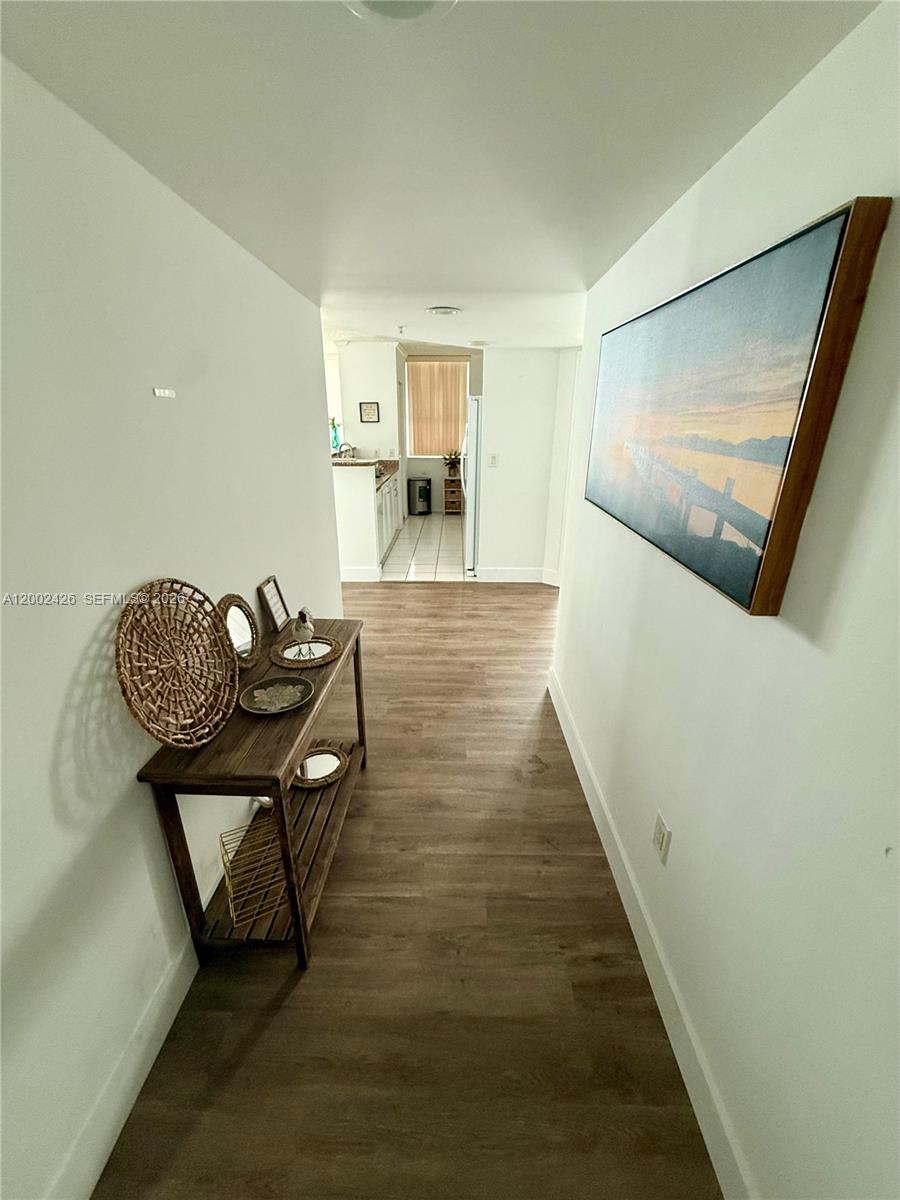 A hallway with wood-look flooring leads to a kitchen with white cabinets and tile floors — 1155 Brickell Bay Dr # 1702, Miami FL 33131, MIAMI, FL