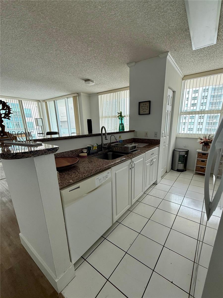A kitchen with white cabinets, granite countertops, and tile flooring overlooks a living area — 1155 Brickell Bay Dr # 1702, Miami FL 33131, MIAMI, FL