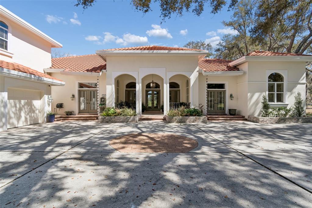 A single-story house with a terracotta tile roof, arched entryway, and a large concrete driveway — 5212 GOLF LINKS BOULEVARD, ZEPHYRHILLS, FL