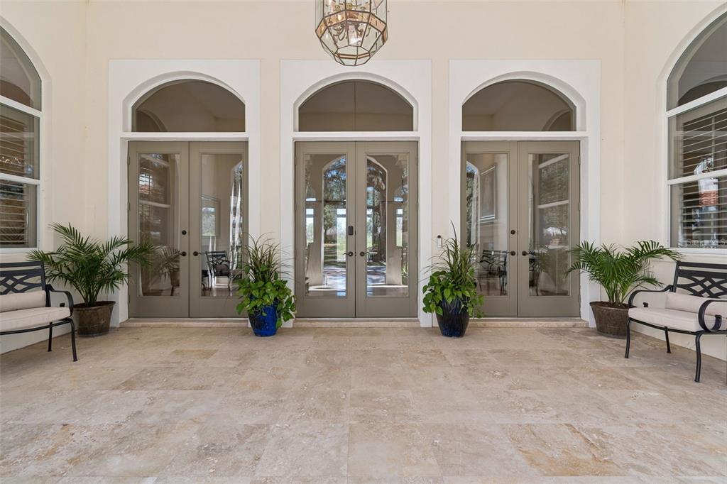 A covered patio features stone flooring, three sets of arched glass doors, and two benches — 5212 GOLF LINKS BOULEVARD, ZEPHYRHILLS, FL