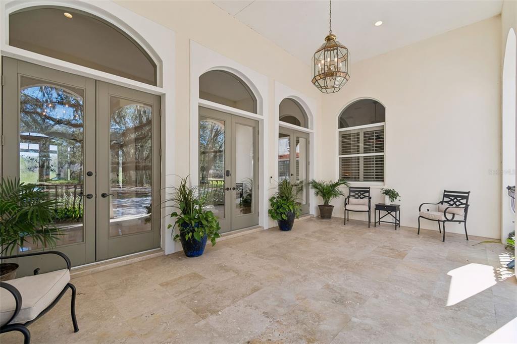 A covered patio features stone tile flooring, arched glass doors, and outdoor seating — 5212 GOLF LINKS BOULEVARD, ZEPHYRHILLS, FL