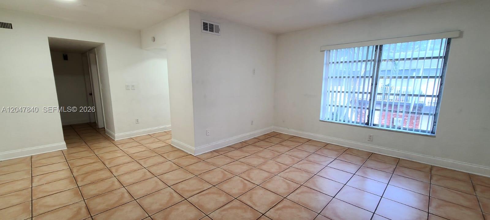 An empty room features beige tile flooring, white walls, and a large window with blinds — 7851 Dunham Blvd # 12, Miami FL 33138, MIAMI, FL