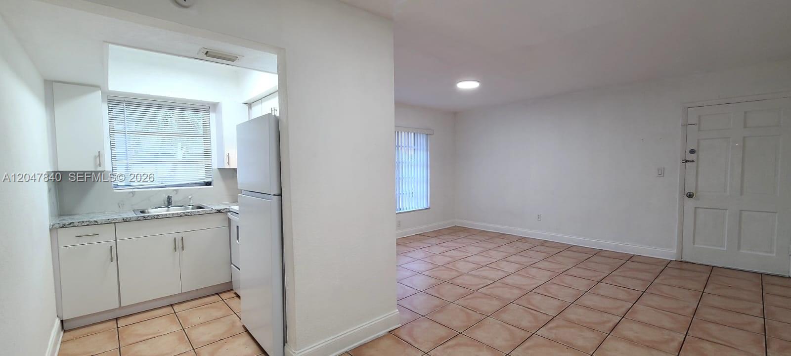 A kitchen with white cabinets and a tiled floor opens into a living area — 7851 Dunham Blvd # 12, Miami FL 33138, MIAMI, FL