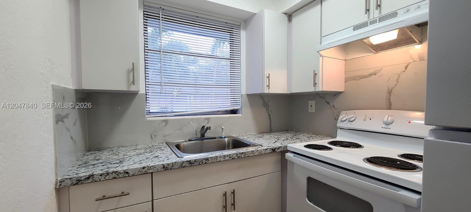 A small kitchen features white cabinets, granite countertops, a stainless steel sink, and white appliances — 7851 Dunham Blvd # 12, Miami FL 33138, MIAMI, FL