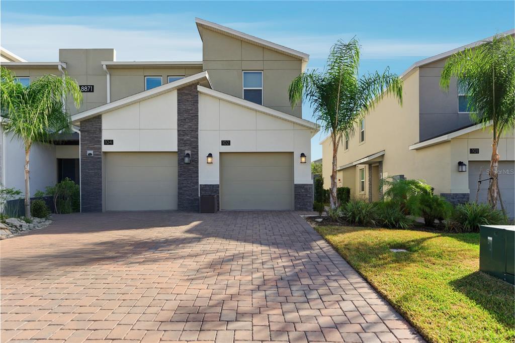 A paved driveway leads to the two-car garages of a modern multi-unit residential building — 8871 CABOT CLIFFS DRIVE UNIT 102, DAVENPORT, FL