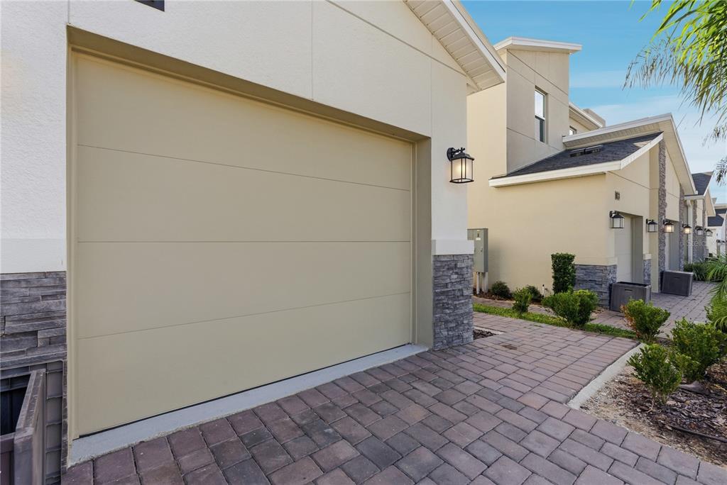 A beige garage door with horizontal panels sits beside a stone-accented exterior and paved driveway — 8871 CABOT CLIFFS DRIVE UNIT 102, DAVENPORT, FL
