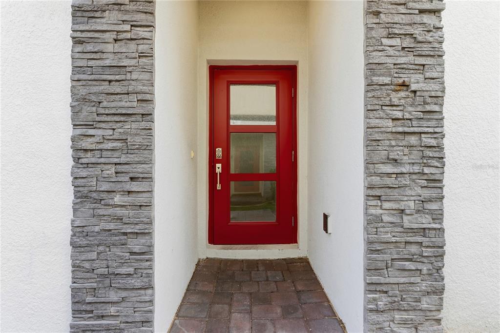 A bright red front door is framed by gray stacked stone columns and white walls — 8871 CABOT CLIFFS DRIVE UNIT 102, DAVENPORT, FL