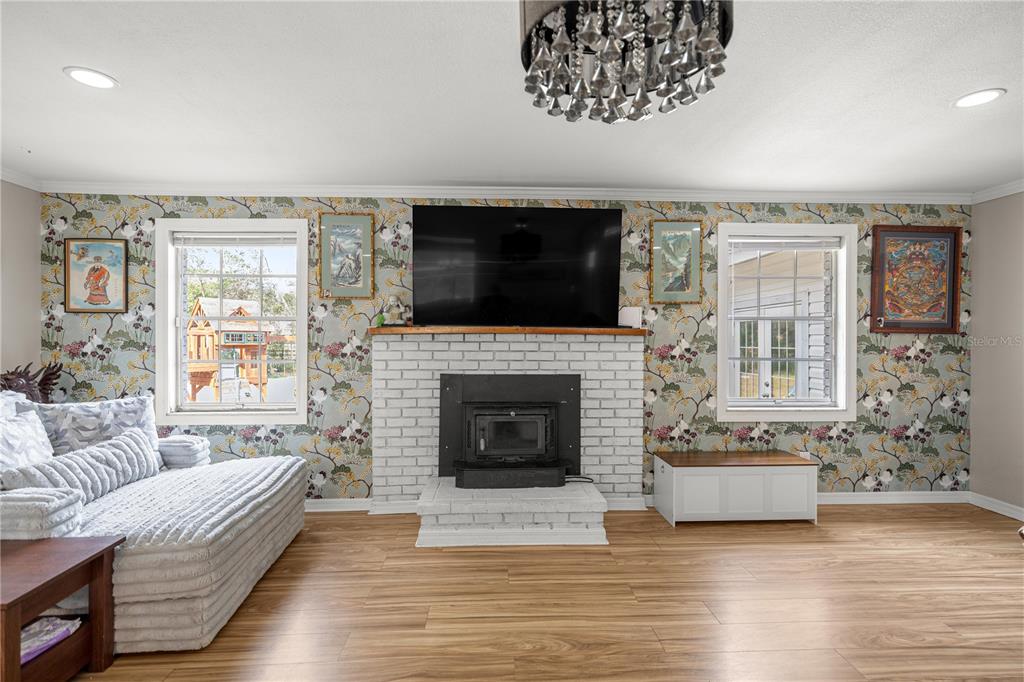 A living room features a white brick fireplace, patterned wallpaper, wood-look flooring, and a crystal chandelier — 5100 SE 44TH AVENUE ROAD, OCALA, FL
