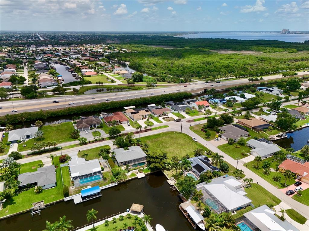 An aerial view shows residential homes along canals near a highway and a large bay — 2014 EVEREST PARKWAY, CAPE CORAL, FL