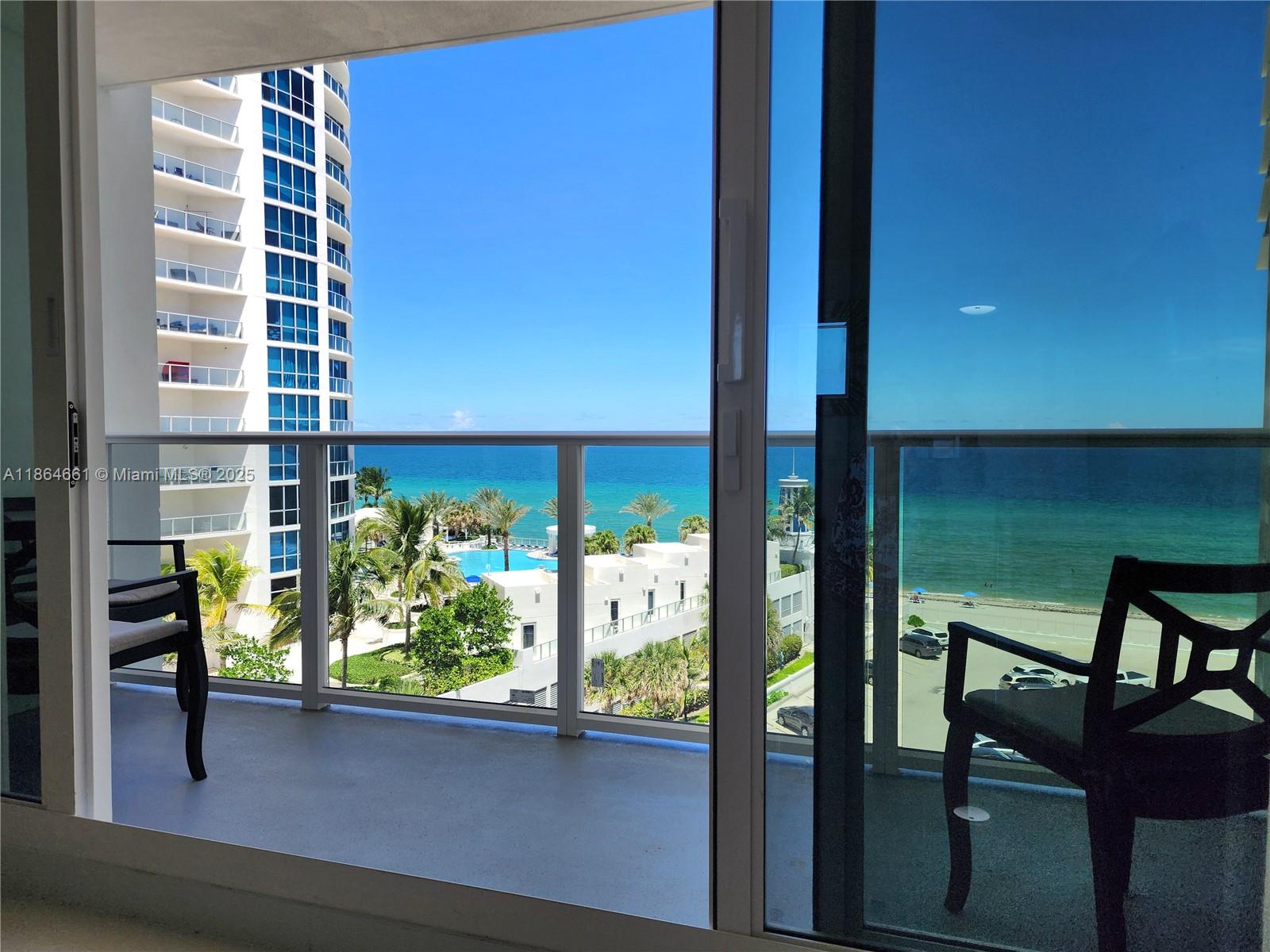 A balcony with two chairs overlooks a swimming pool, beach, and the ocean — 3505 S Ocean Dr # 707, Hollywood FL 33019, HOLLYWOOD, FL