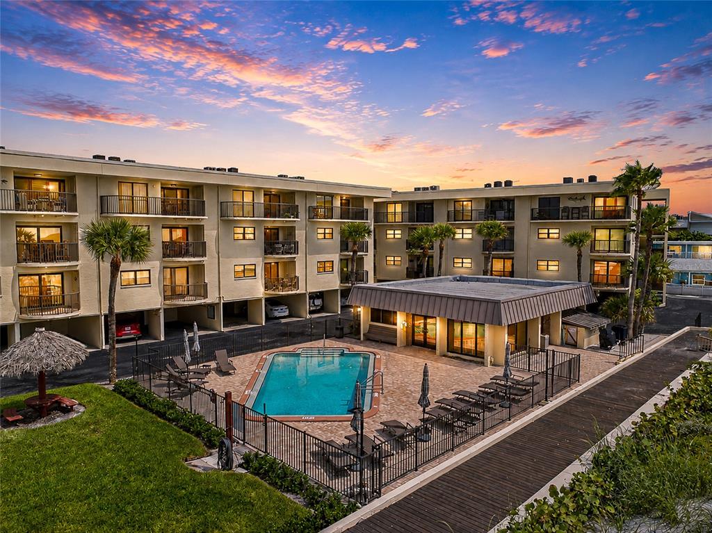 An outdoor swimming pool sits in the courtyard of a multi-story apartment complex at sunset — 3500 GULF BOULEVARD UNIT 204, BELLEAIR BEACH, FL