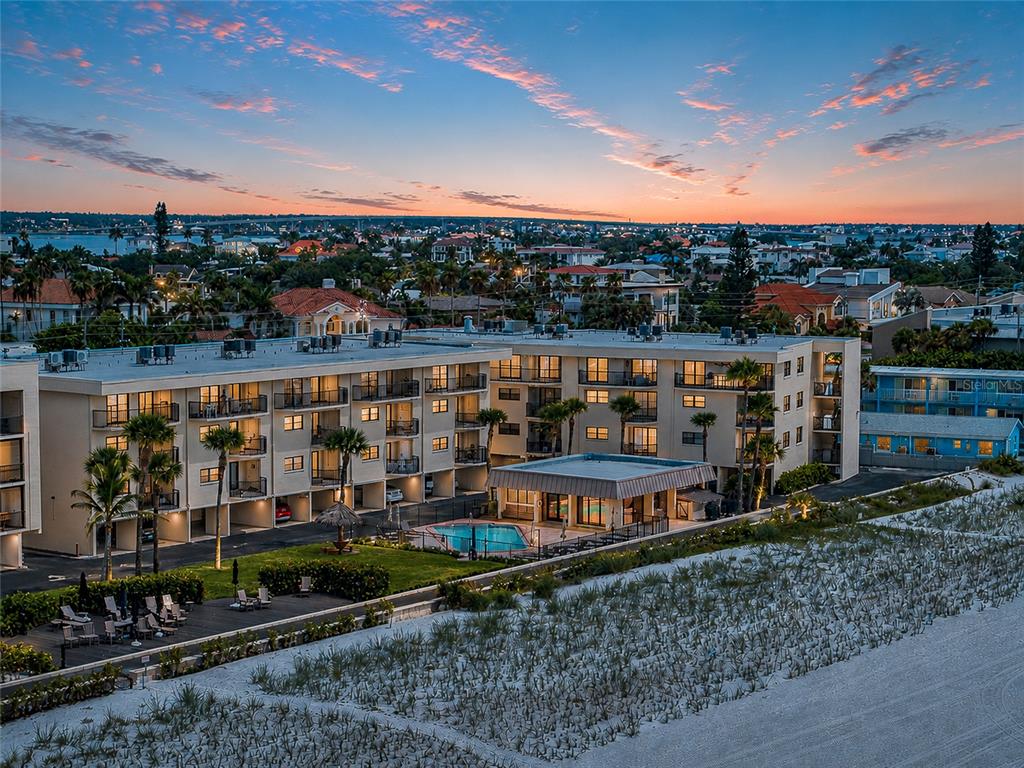 An aerial view shows a multi-story apartment building with a pool near a sandy beach — 3500 GULF BOULEVARD UNIT 204, BELLEAIR BEACH, FL