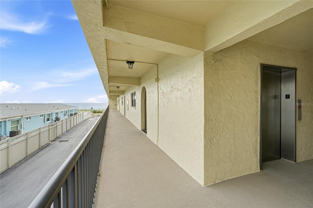 An outdoor walkway features a metal railing, a beige stucco wall, and an elevator entrance — 3500 GULF BOULEVARD UNIT 204, BELLEAIR BEACH, FL