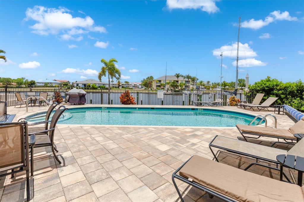 A swimming pool with lounge chairs on a paved patio overlooking a canal and marina — 3221 WHITE IBIS COURT UNIT C1, PUNTA GORDA, FL