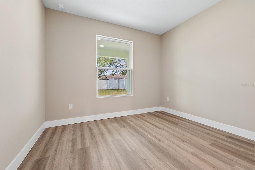 An empty room features light beige walls, white trim, and wood-look flooring with a window — 21 POSTMAN LANE, PALM COAST, FL