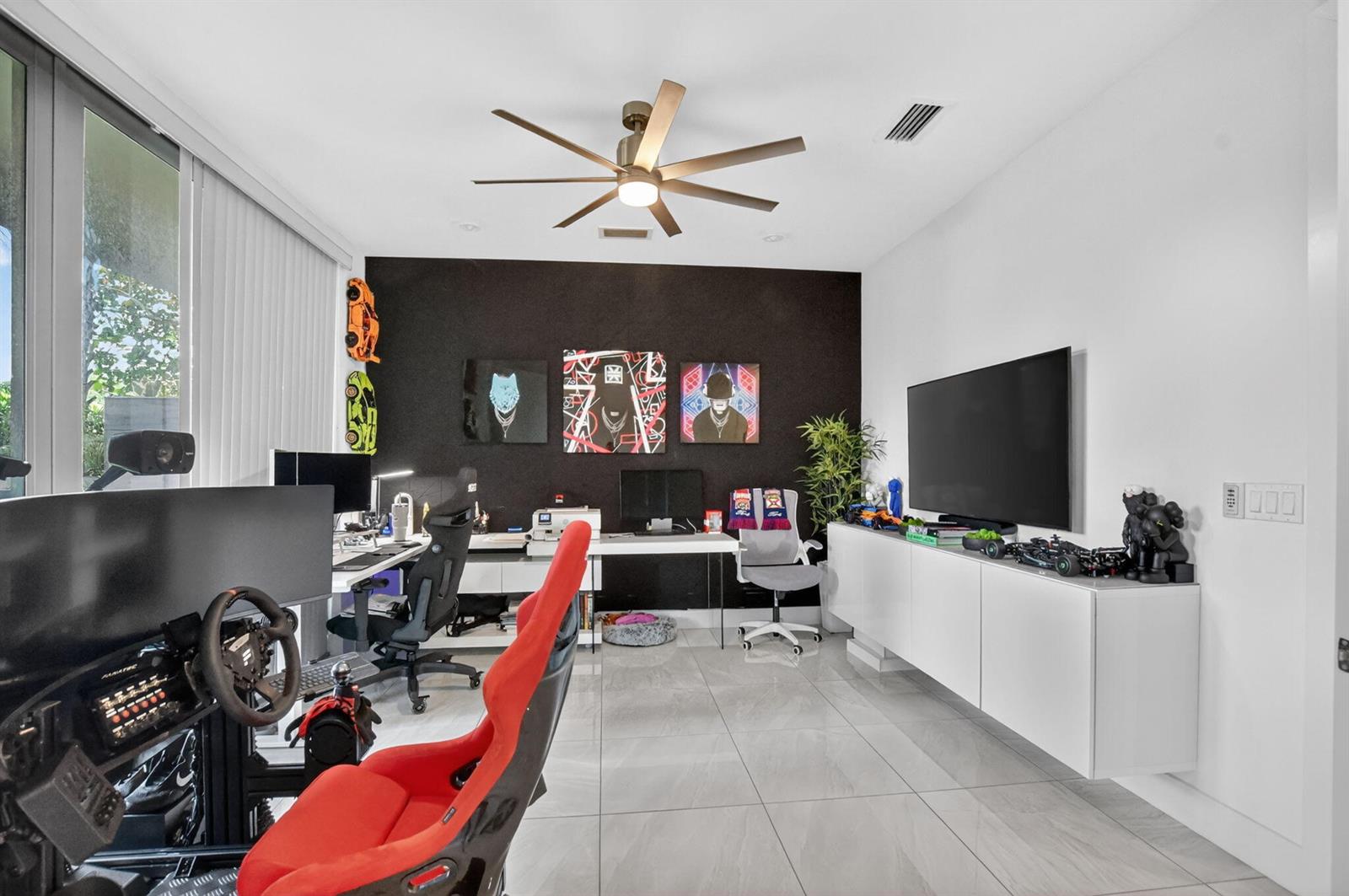 A modern home office features a racing simulator, dual desks, a wall-mounted television, and tile flooring — 4021 NW 18th Way, Boca Raton FL 33431, BOCA RATON, FL