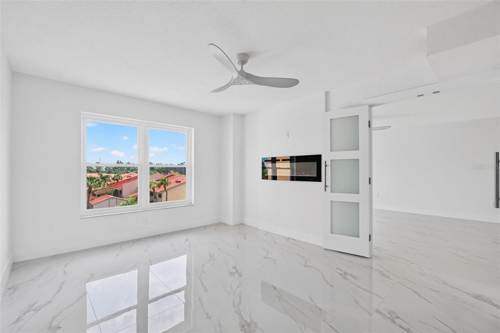 A bright room with white marble-look tile floors, a ceiling fan, and a wall-mounted fireplace — 4900 BRITTANY DRIVE S UNIT 405, ST PETERSBURG, FL