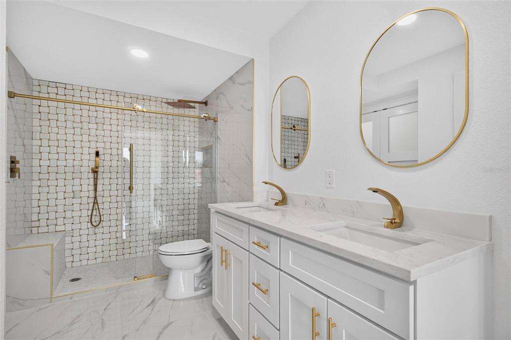 A modern bathroom features a double vanity with gold fixtures, marble countertops, and a glass-enclosed shower — 4900 BRITTANY DRIVE S UNIT 405, ST PETERSBURG, FL