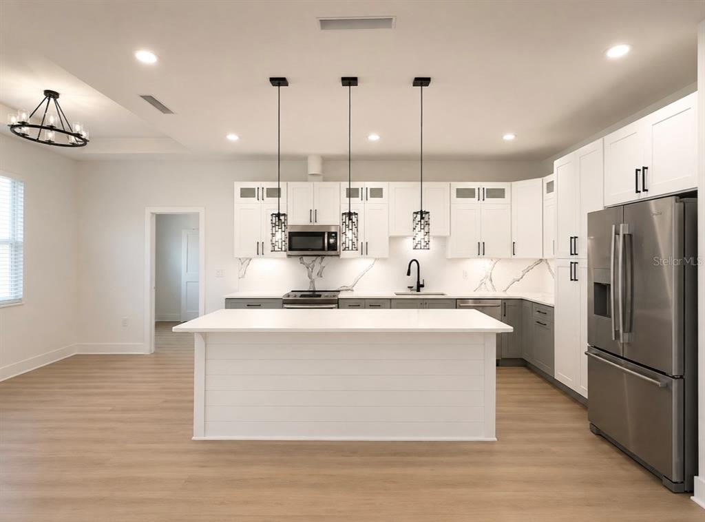 A modern kitchen features white upper cabinets, gray lower cabinets, a central island, and stainless appliances — 1064 MONROE AVENUE, BROOKSVILLE, FL