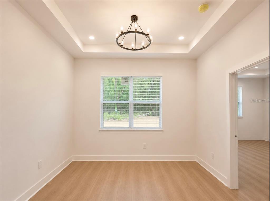 An empty room with light wood-look flooring, a tray ceiling, and a central chandelier — 1064 MONROE AVENUE, BROOKSVILLE, FL