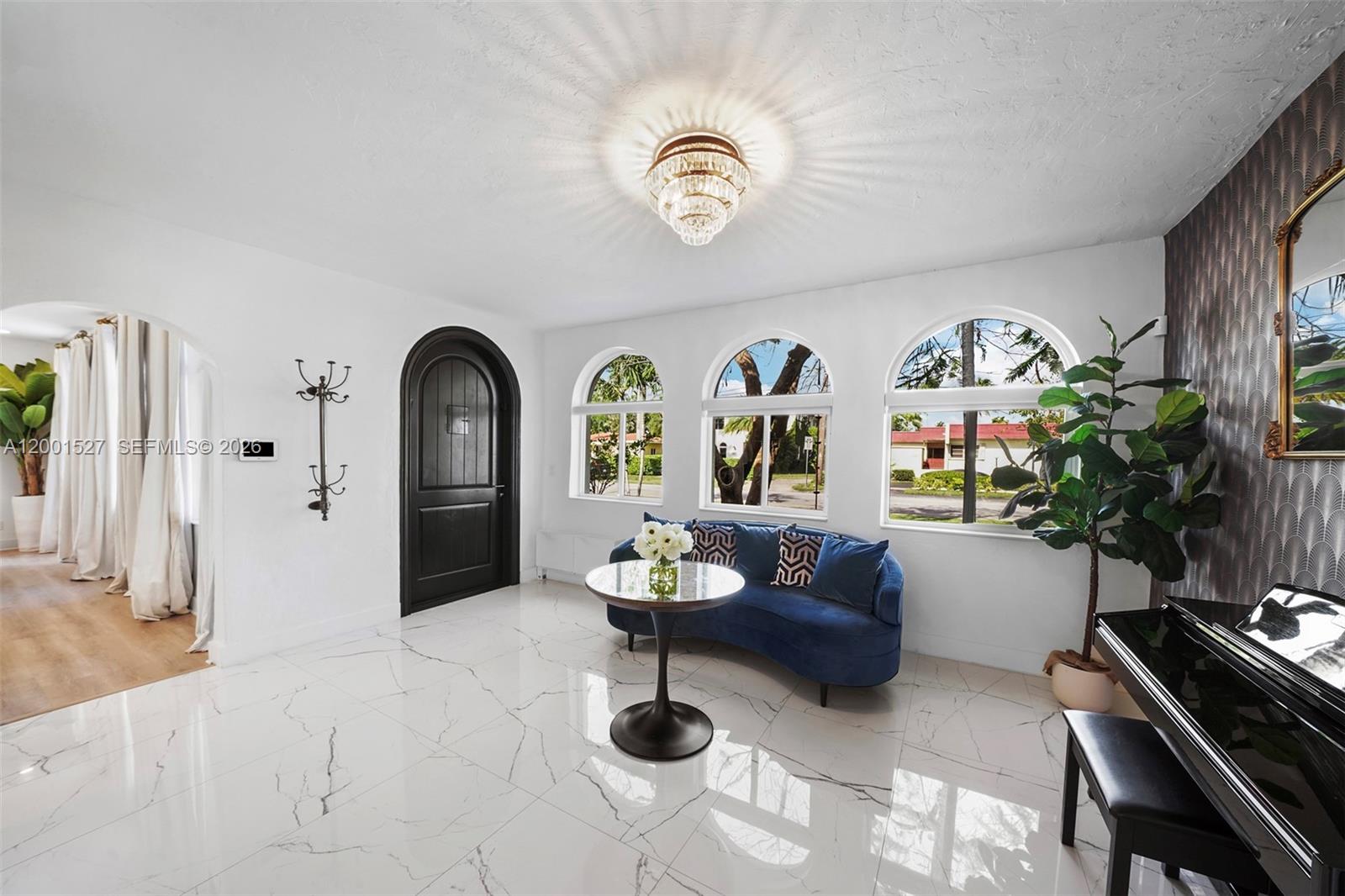 A bright foyer features white marble floors, an arched black door, and a blue sofa — 5237 La Gorce Drive # 5237, Miami Beach FL 33140, MIAMI BEACH, FL