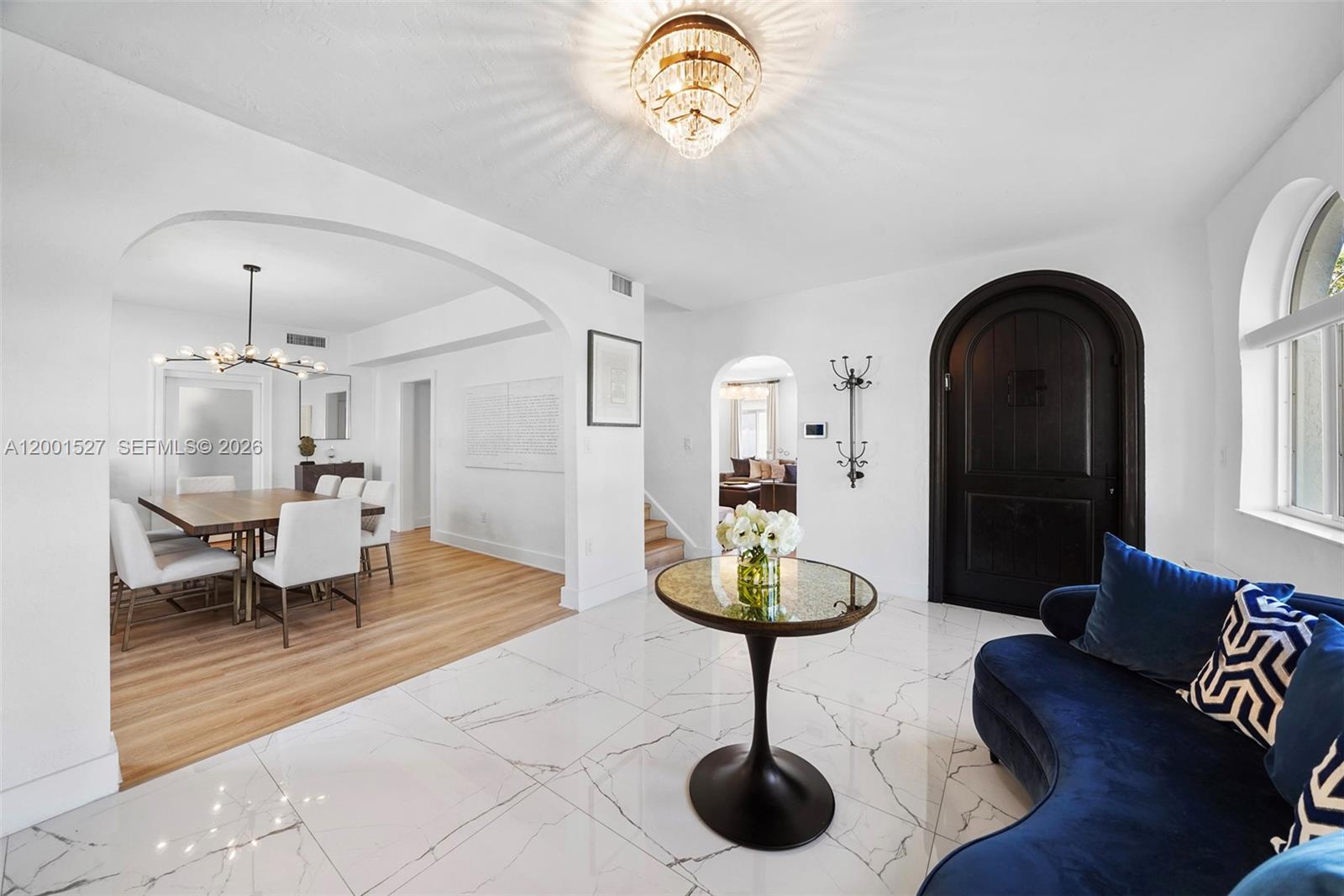 An entryway with white marble floors, a blue sofa, and an arched doorway leads to a dining area — 5237 La Gorce Drive # 5237, Miami Beach FL 33140, MIAMI BEACH, FL