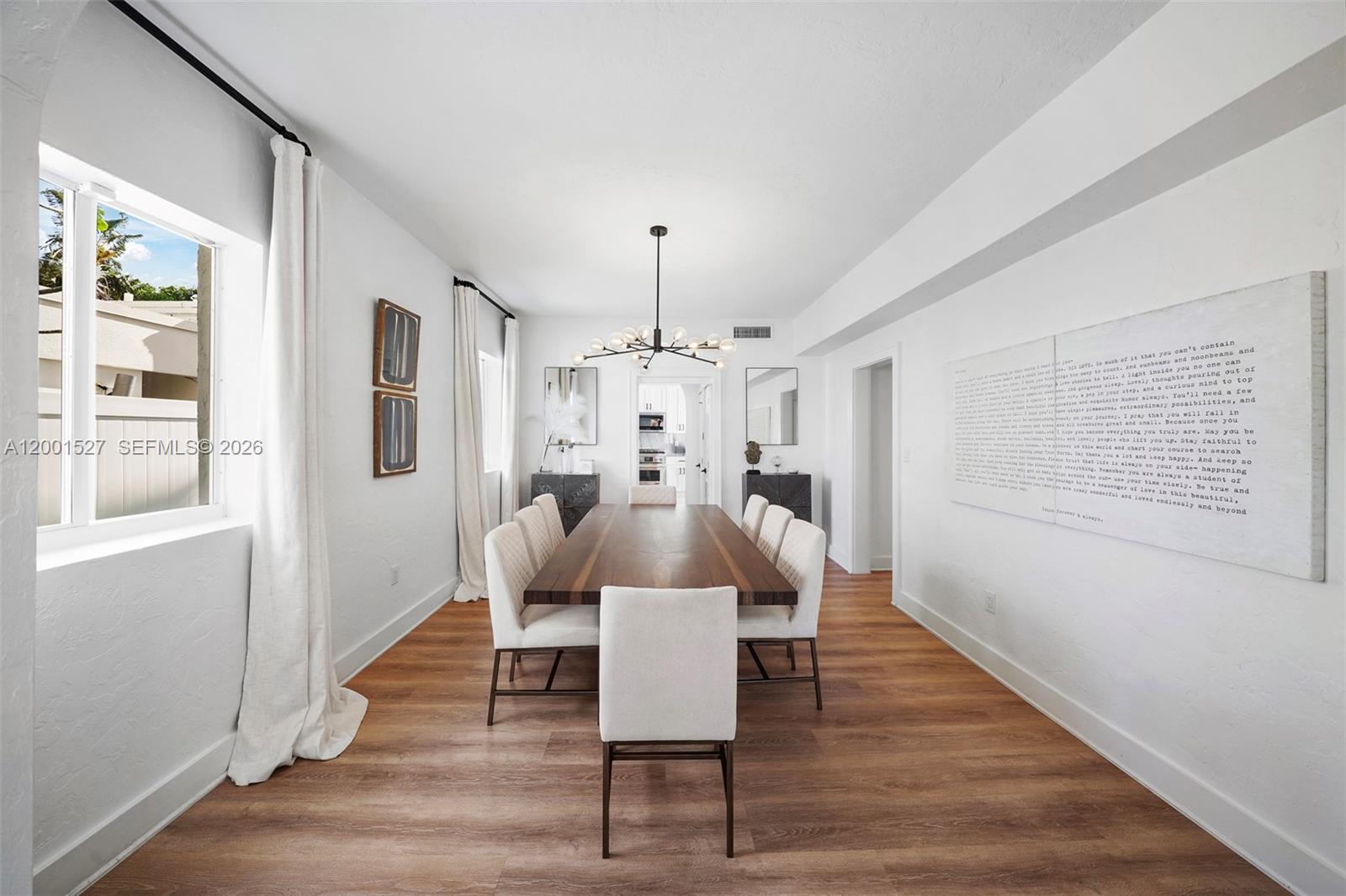 A dining room features a long wooden table, white upholstered chairs, and a modern chandelier — 5237 La Gorce Drive # 5237, Miami Beach FL 33140, MIAMI BEACH, FL