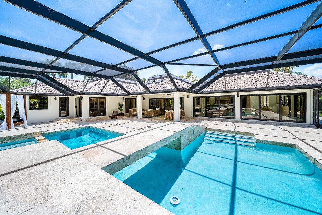 A screened-in patio featuring a swimming pool, a hot tub, and light-colored stone decking — 1648 Breakers West Boulevard, West Palm Beach FL 33411, WEST PALM BEACH, FL