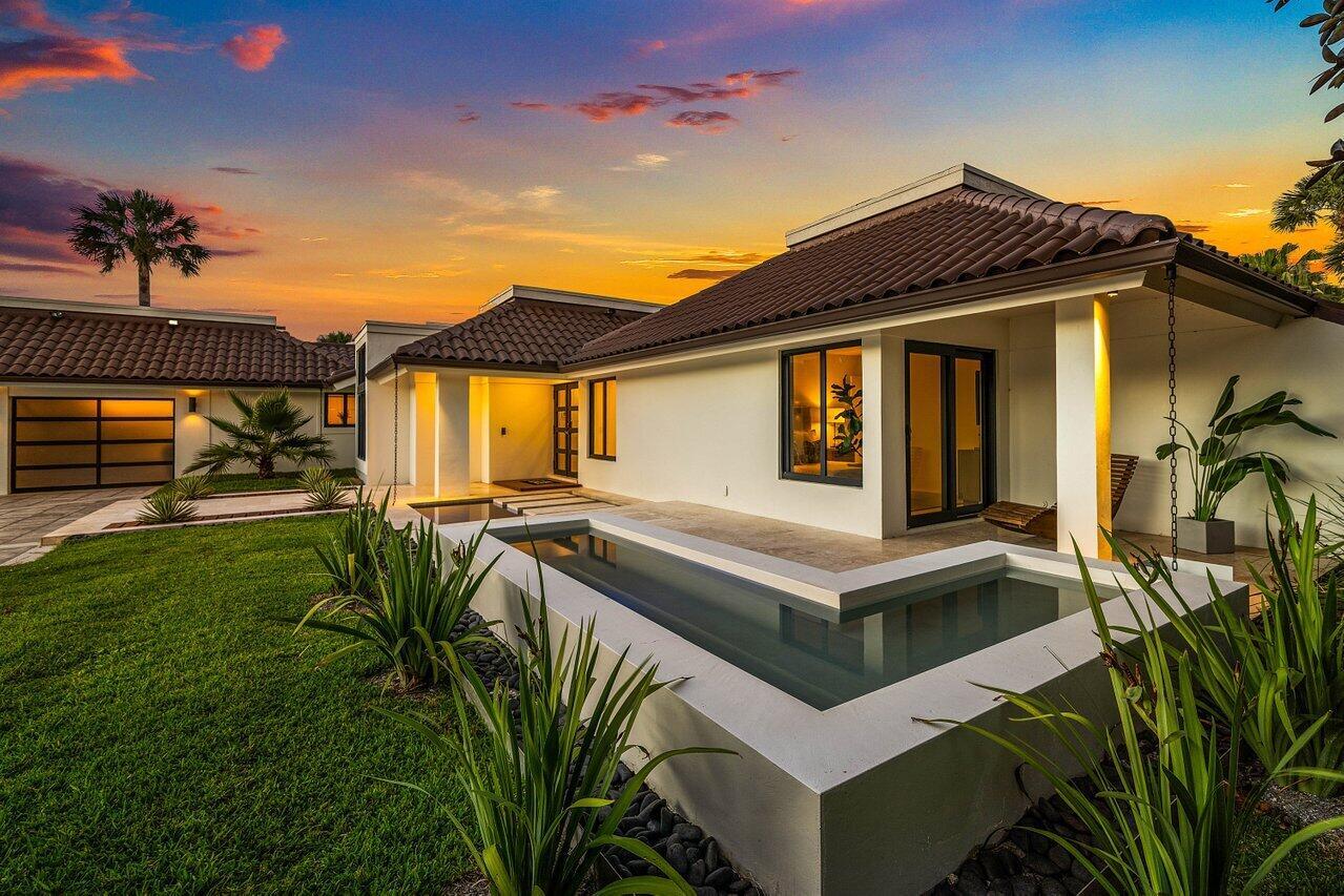 A modern house exterior features a raised L-shaped pool, white stucco walls, and tiled roof — 1648 Breakers West Boulevard, West Palm Beach FL 33411, WEST PALM BEACH, FL