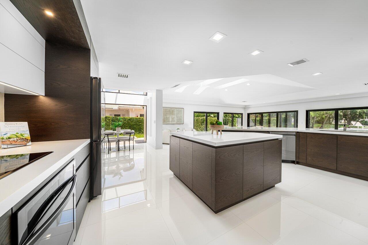 A modern kitchen features a large dark wood island, white countertops, and glossy tile floors — 1648 Breakers West Boulevard, West Palm Beach FL 33411, WEST PALM BEACH, FL