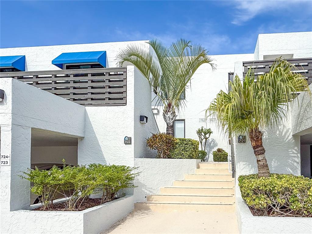A white stucco building exterior features a staircase, palm trees, and blue window awnings — 724 BAYPORT WAY UNIT 724, LONGBOAT KEY, FL