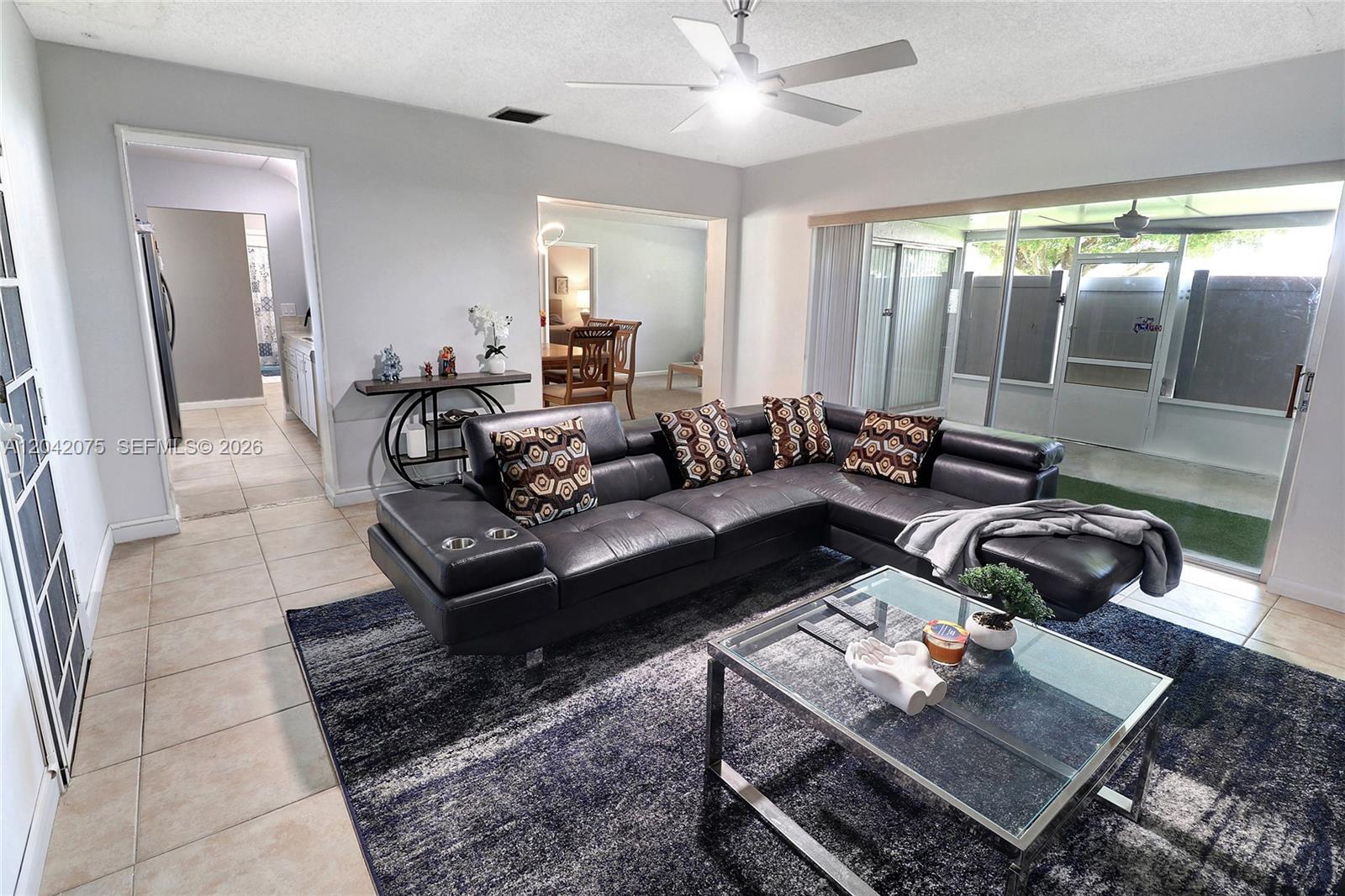 A living room features a black leather sectional, a glass coffee table, and tile flooring — 14771 Wildflower Ln, Delray Beach FL 33446, DELRAY BEACH, FL