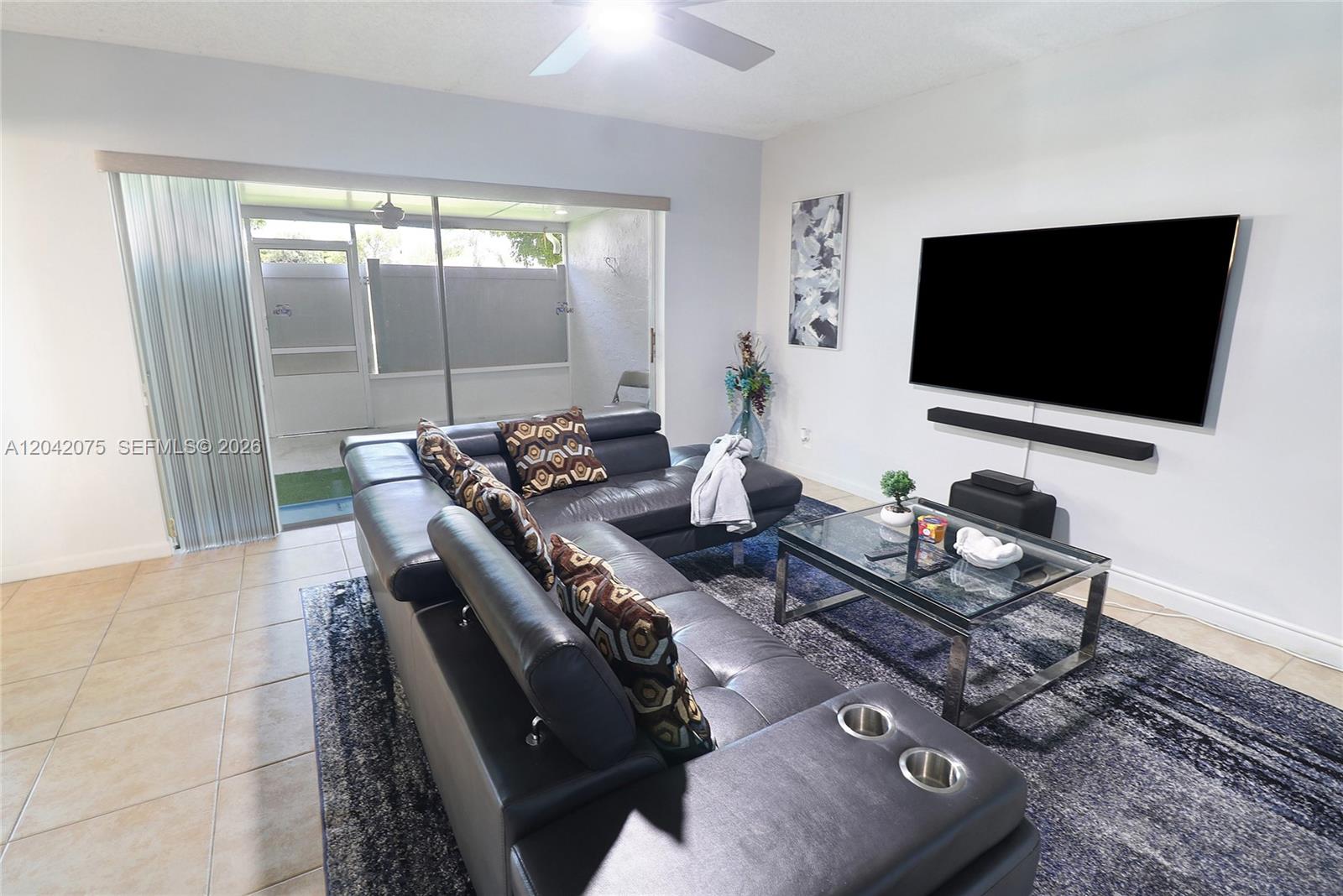 A living room features a dark leather sectional, glass coffee table, and a wall-mounted television — 14771 Wildflower Ln, Delray Beach FL 33446, DELRAY BEACH, FL