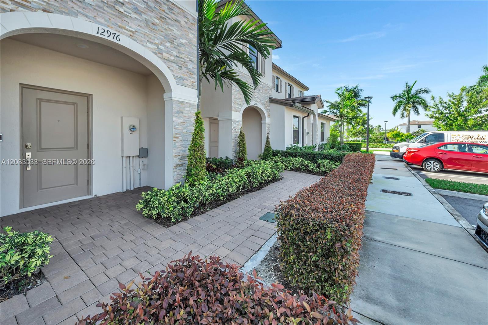 The exterior of a two-story residential building features a stone facade, arched entryway, and landscaping — 12976 SW 233rd Ter, Homestead FL 33032, HOMESTEAD, FL
