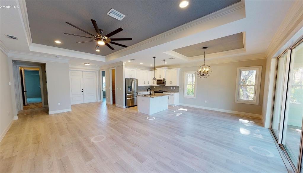 A spacious open-concept kitchen and living area features light wood flooring and a tray ceiling — 6782 PAIGO LANE, NORTH PORT, FL