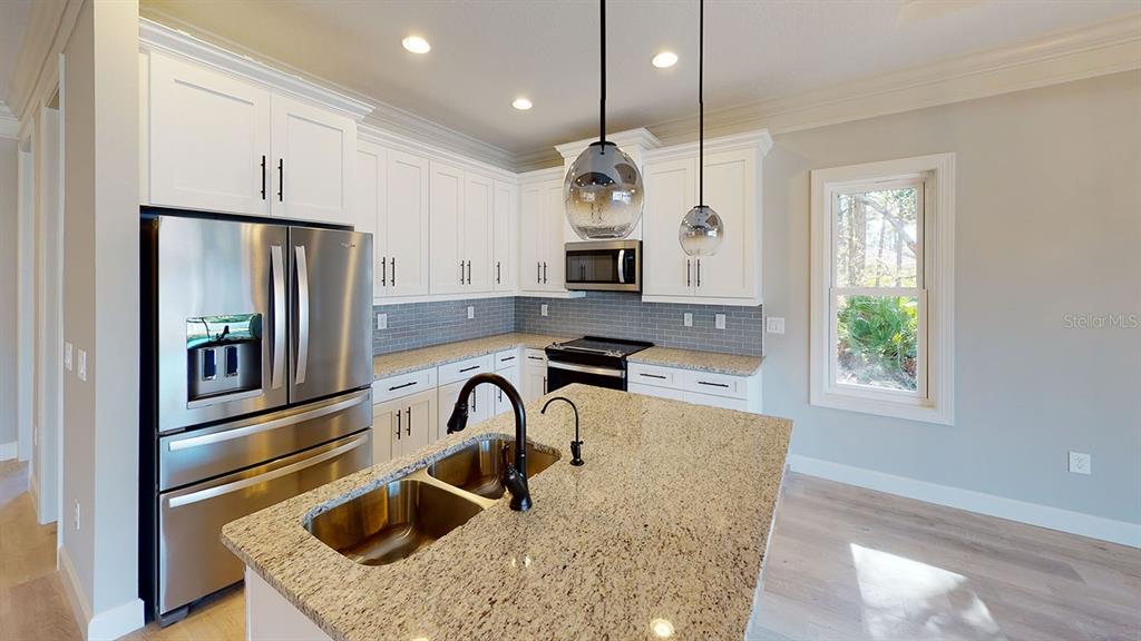 A kitchen features white cabinets, granite countertops, a stainless steel refrigerator, and a center island — 6782 PAIGO LANE, NORTH PORT, FL