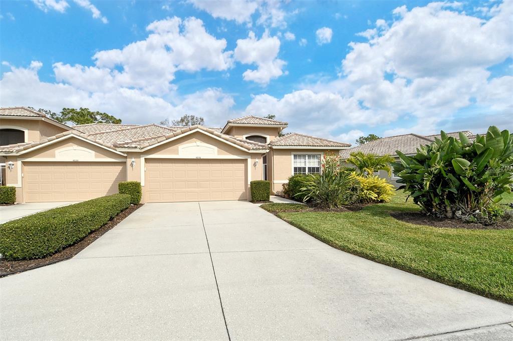 A beige house with a two-car garage, a concrete driveway, and manicured landscaping — 4516 LEGACY COURT, SARASOTA, FL