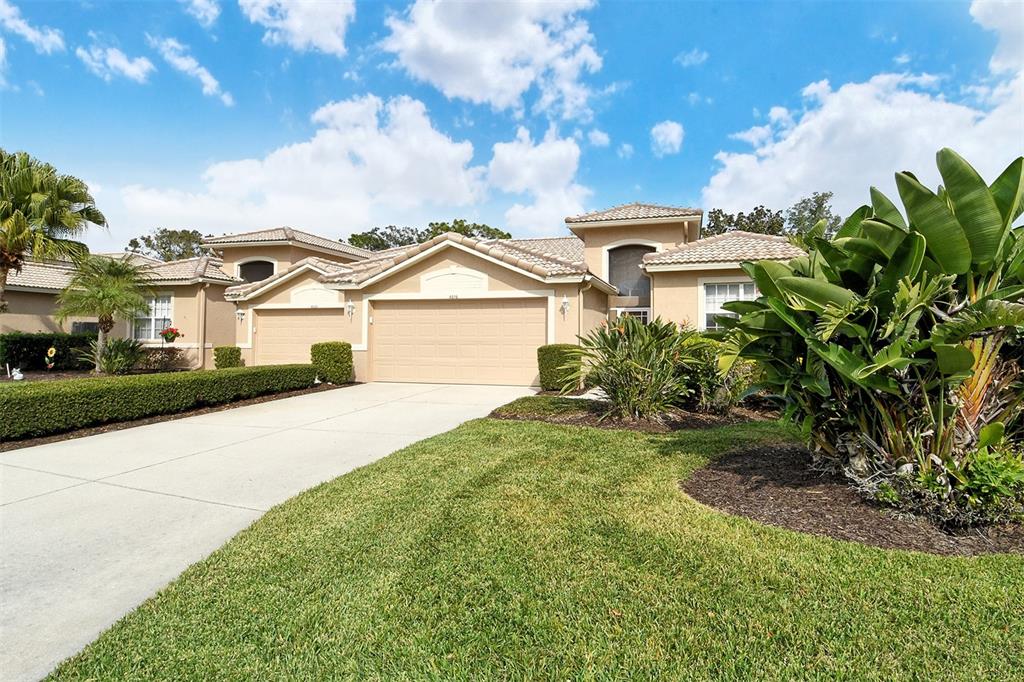 A beige single-story house with a multi-car garage, tile roof, and landscaped front yard — 4516 LEGACY COURT, SARASOTA, FL