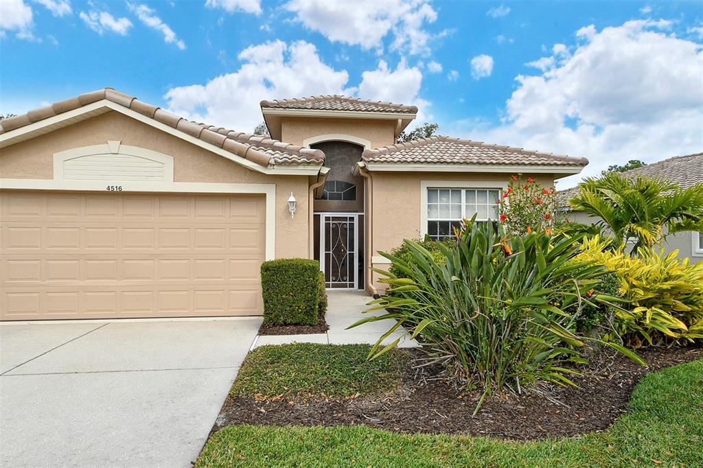 A single-story house with a beige stucco exterior, a two-car garage, and tropical landscaping — 4516 LEGACY COURT, SARASOTA, FL