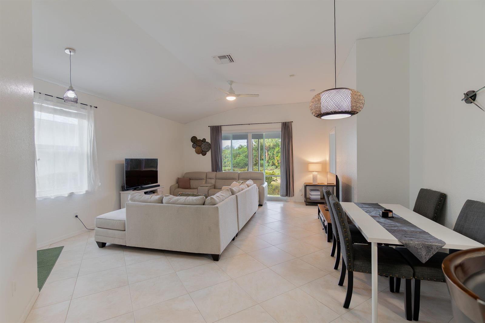 An open-concept living and dining area features tile flooring, a sectional sofa, and sliding doors — 115 Coconut Key Lane, Delray Beach FL 33484, DELRAY BEACH, FL