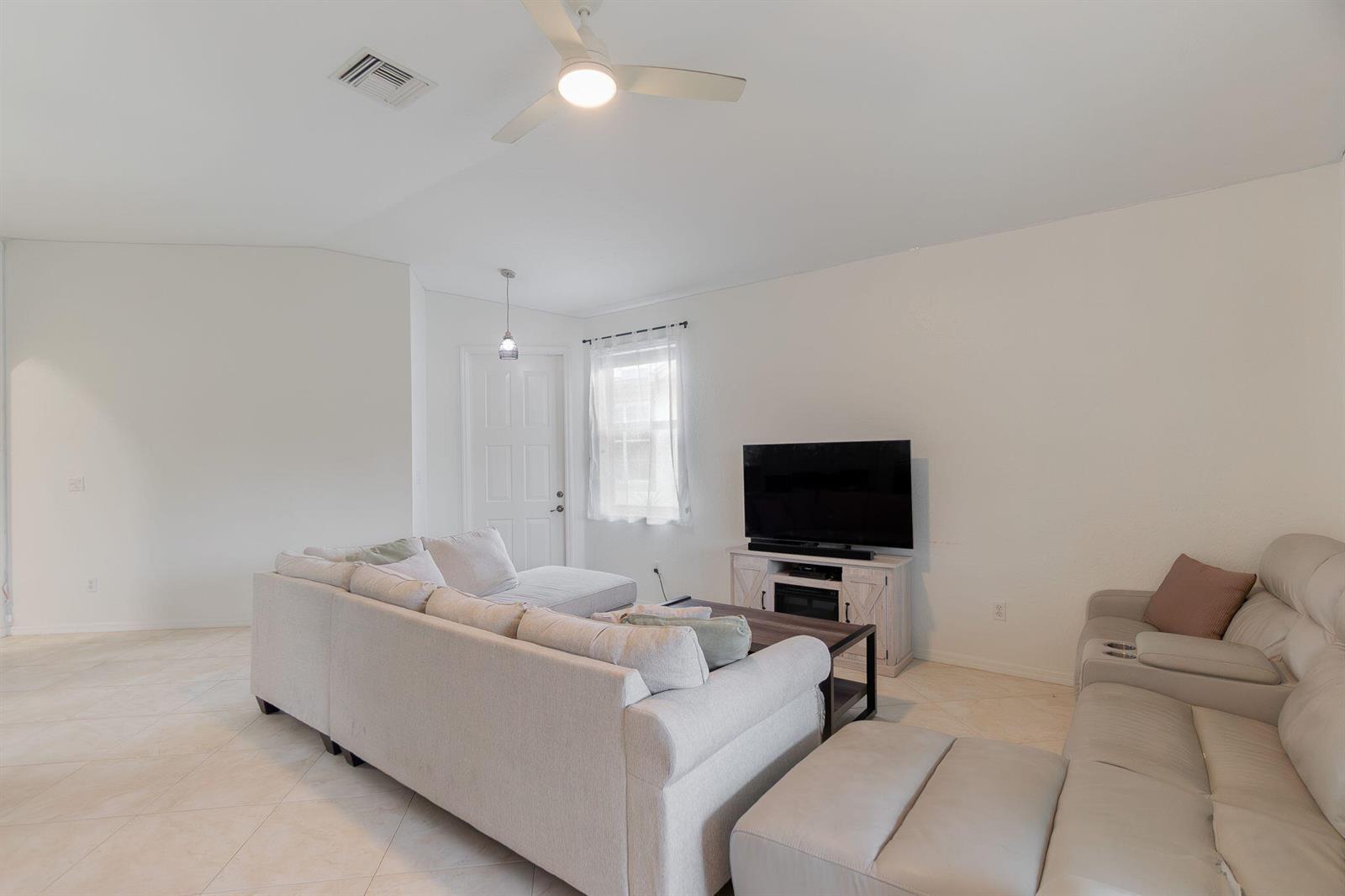 A living room features a sectional sofa, a television on a console, and tile flooring — 115 Coconut Key Lane, Delray Beach FL 33484, DELRAY BEACH, FL