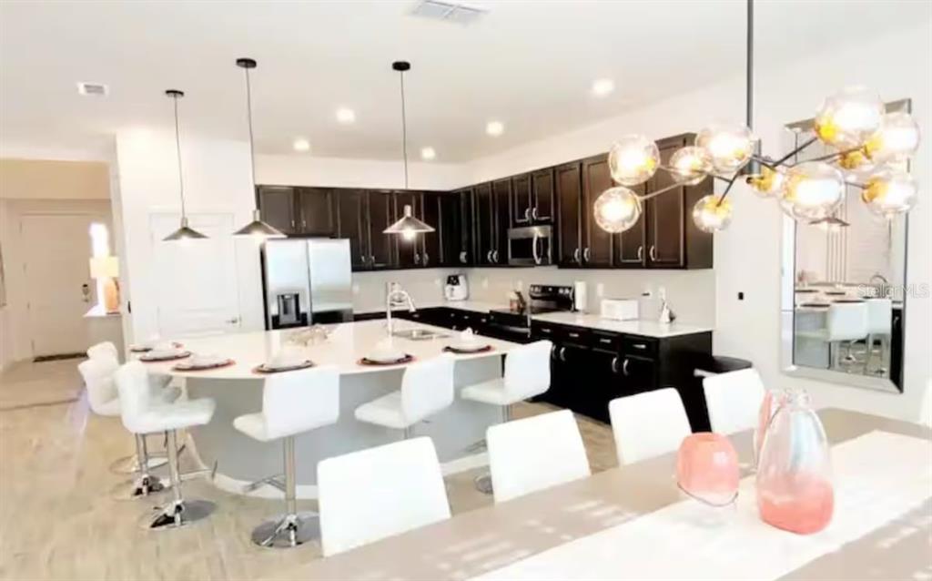 A modern kitchen features dark cabinets, a large curved island with white stools, and pendant lighting — 2484 SHANTI DRIVE, KISSIMMEE, FL