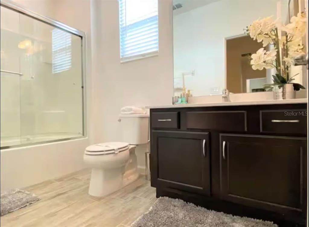 A bathroom features a dark wood vanity, a toilet, and a glass-enclosed shower — 2484 SHANTI DRIVE, KISSIMMEE, FL