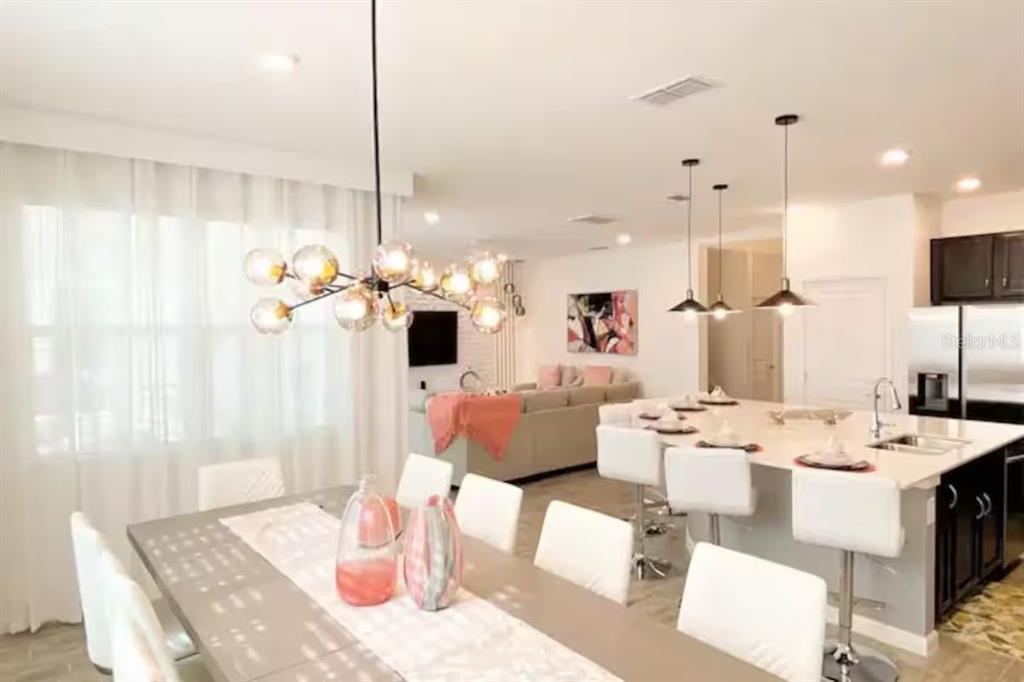 An open-concept dining and kitchen area features a modern chandelier, white barstools, and neutral decor — 2484 SHANTI DRIVE, KISSIMMEE, FL