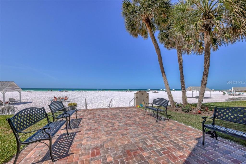 A brick patio with three metal benches overlooks a white sand beach and ocean — 6154 MIDNIGHT PASS ROAD UNIT A06, SARASOTA, FL