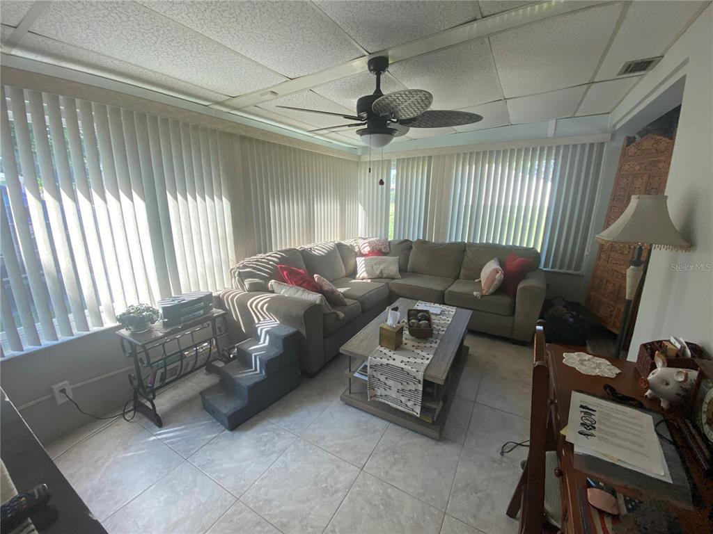 A sunroom features tile flooring, a sectional sofa, a coffee table, and vertical window blinds — 1609 WHITEBRIDGE DRIVE UNIT C, PALM HARBOR, FL