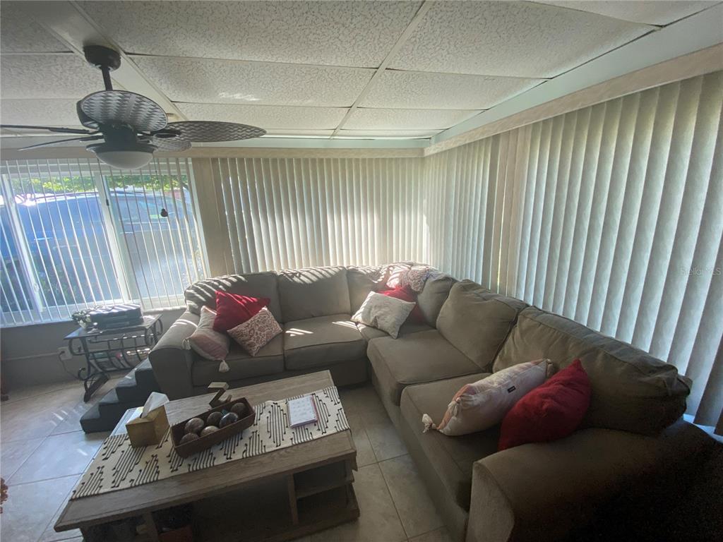A sunroom features a large sectional sofa, a coffee table, and vertical blinds on windows — 1609 WHITEBRIDGE DRIVE UNIT C, PALM HARBOR, FL